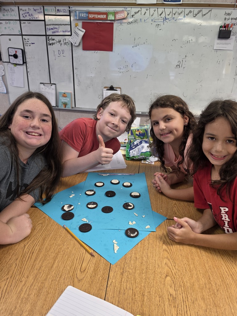 Four children sit around a table with a blue game board. They are smiling.