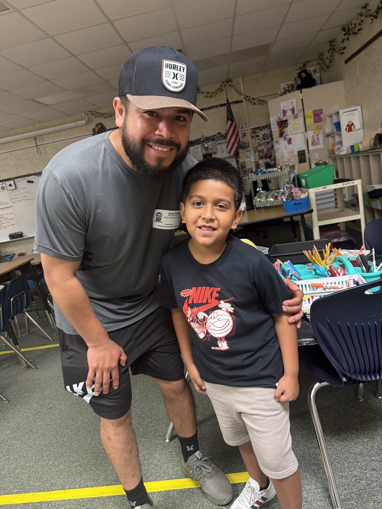 A smiling man and a boy in a classroom with desks and chairs in the background.