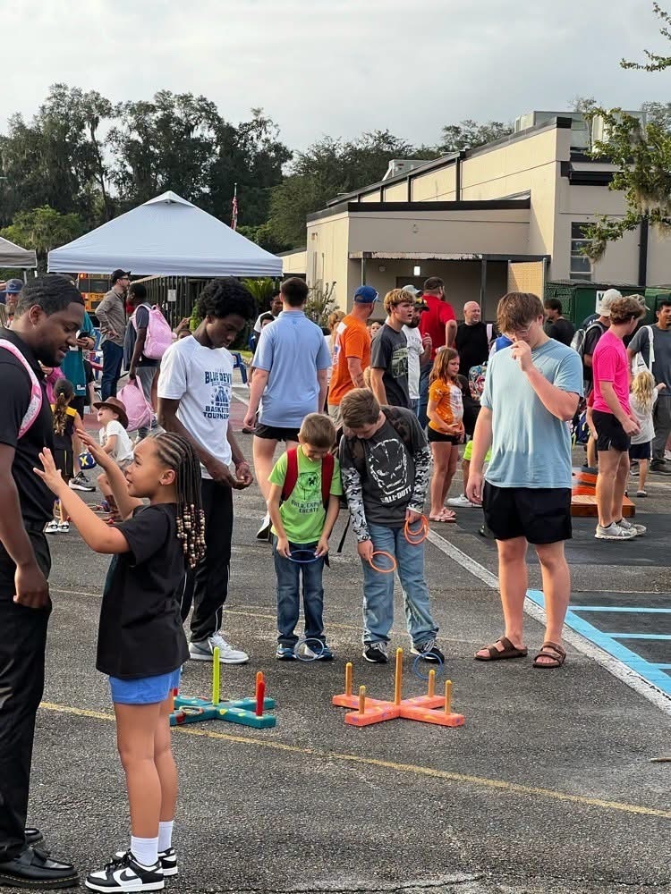 A group of people in a parking lot. Some children are playing with toy rings. A white tent is in the background.