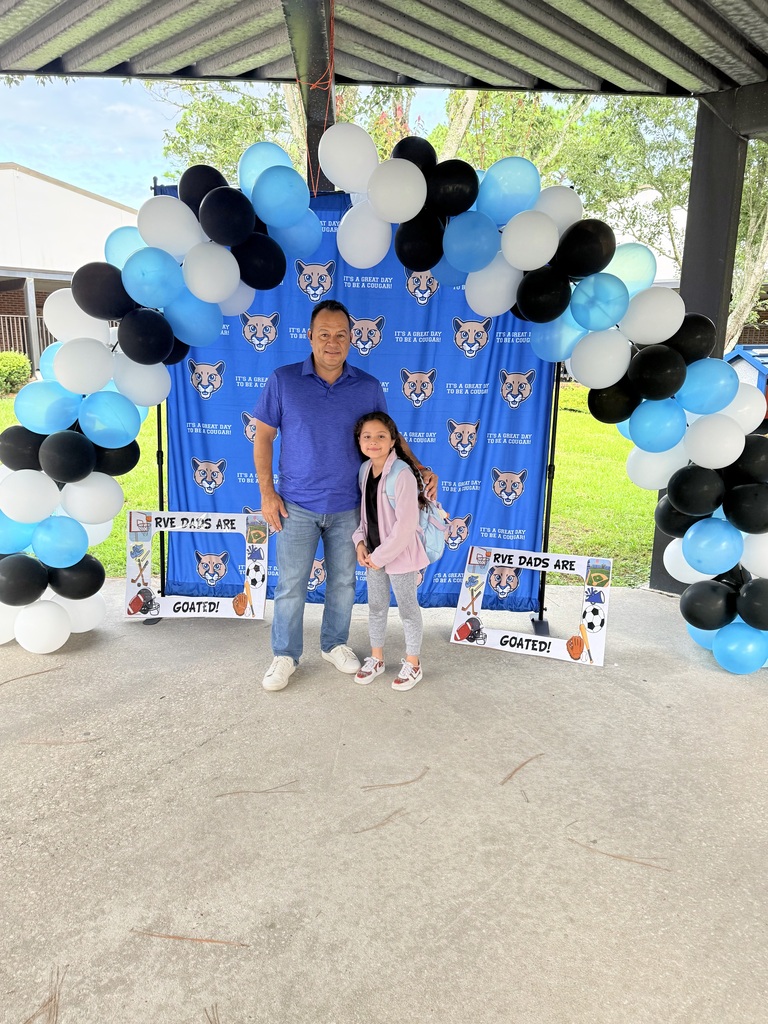 Dad and child stand in front of the school backdrop.