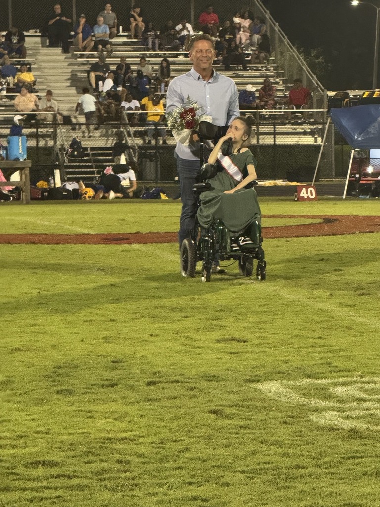 Man with a young person in a wheelchair on a field with spectators in stands.