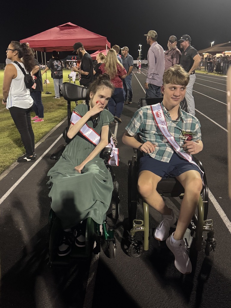 A boy and a girl in wheelchairs wear sashes and pose for a photo on a track.