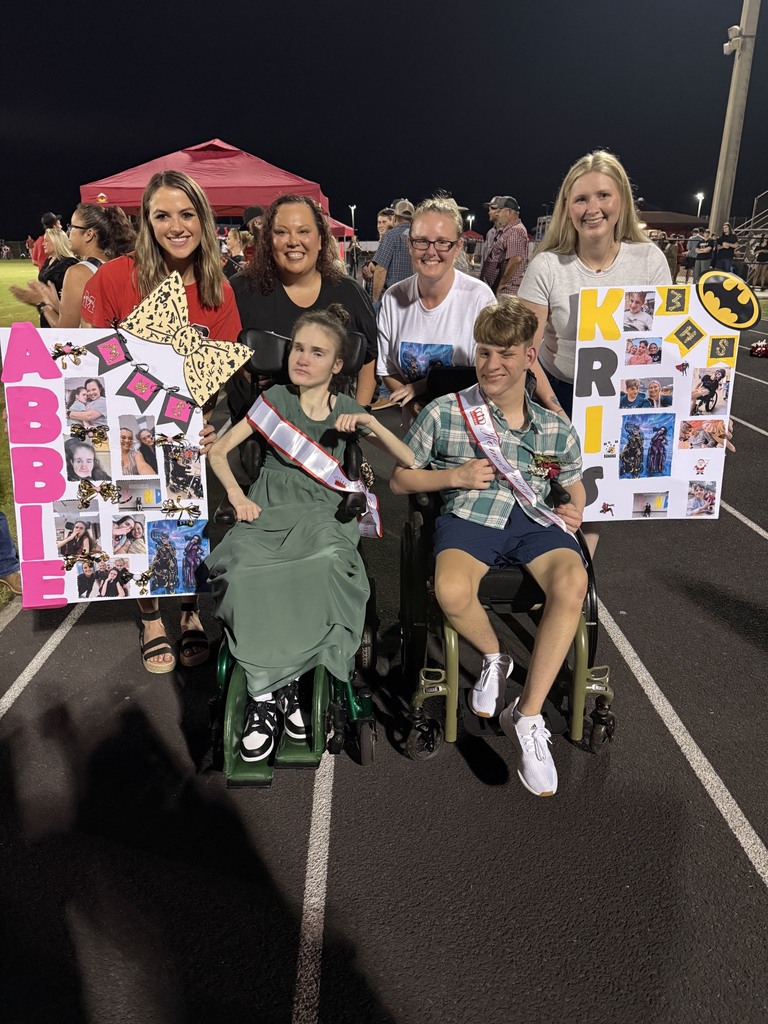 Five people on a track hold signs, with two in wheelchairs. They smile and pose for a photo at night.