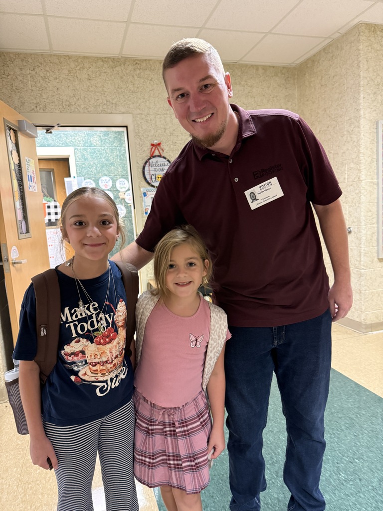 Man in dark shirt and dark pants with two girls in hallway; one girl with backpack and other with pink top.