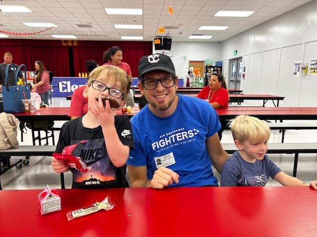 Three children at a red table. Two boys wear glasses, the man next to them wears a blue shirt with "FIGHTERS" written on it.
