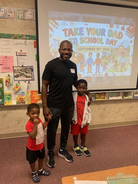 Man with two young children in a classroom with a projector screen in the background.