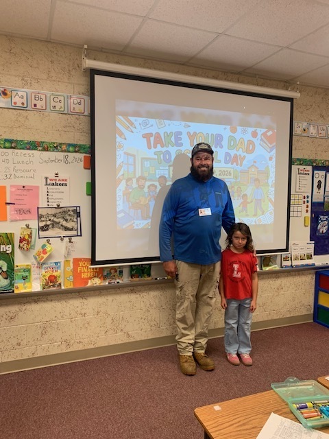 Man and child standing in front of a projector screen with a slide reading "Take Your Dad 30...Day".