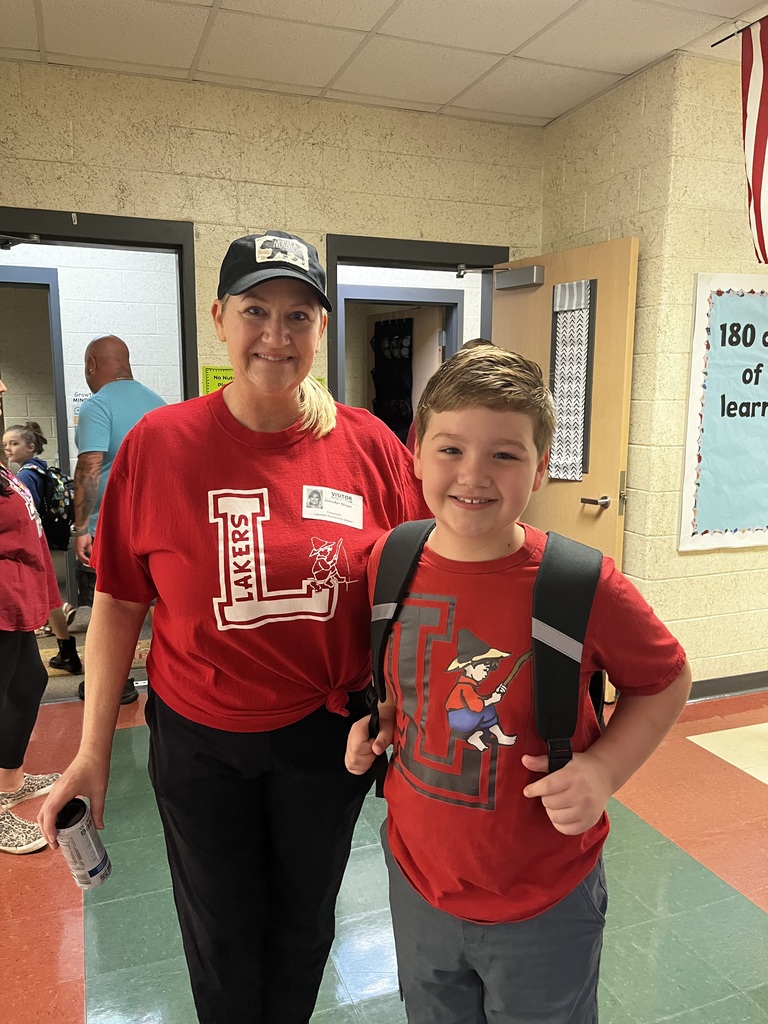 A woman and a young boy stand in a hallway. Both wear red shirts, one with "LAKESIDE" and the other with a cartoon character.