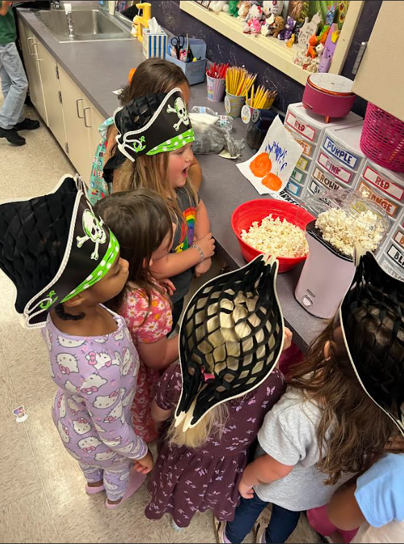 Children in pirate hats surround a popcorn machine at a kitchen counter. Bowls of popcorn are on the counter.