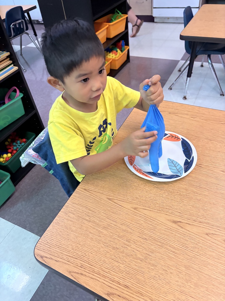 A young boy in a yellow shirt is seated at a table, holding a blue glove.