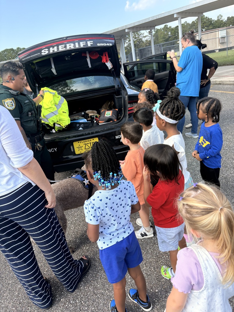 Police officer showing children a car with its trunk open in a parking lot. 