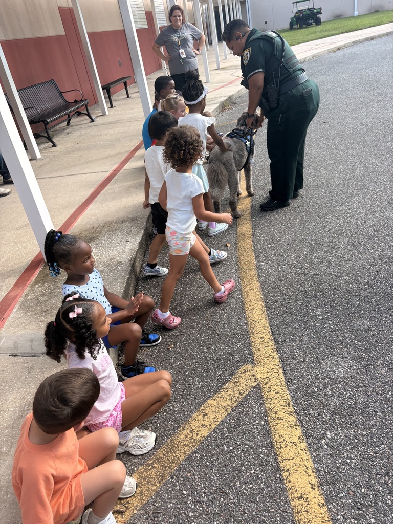 Kids sit on a curb with a police officer and  dog. 
