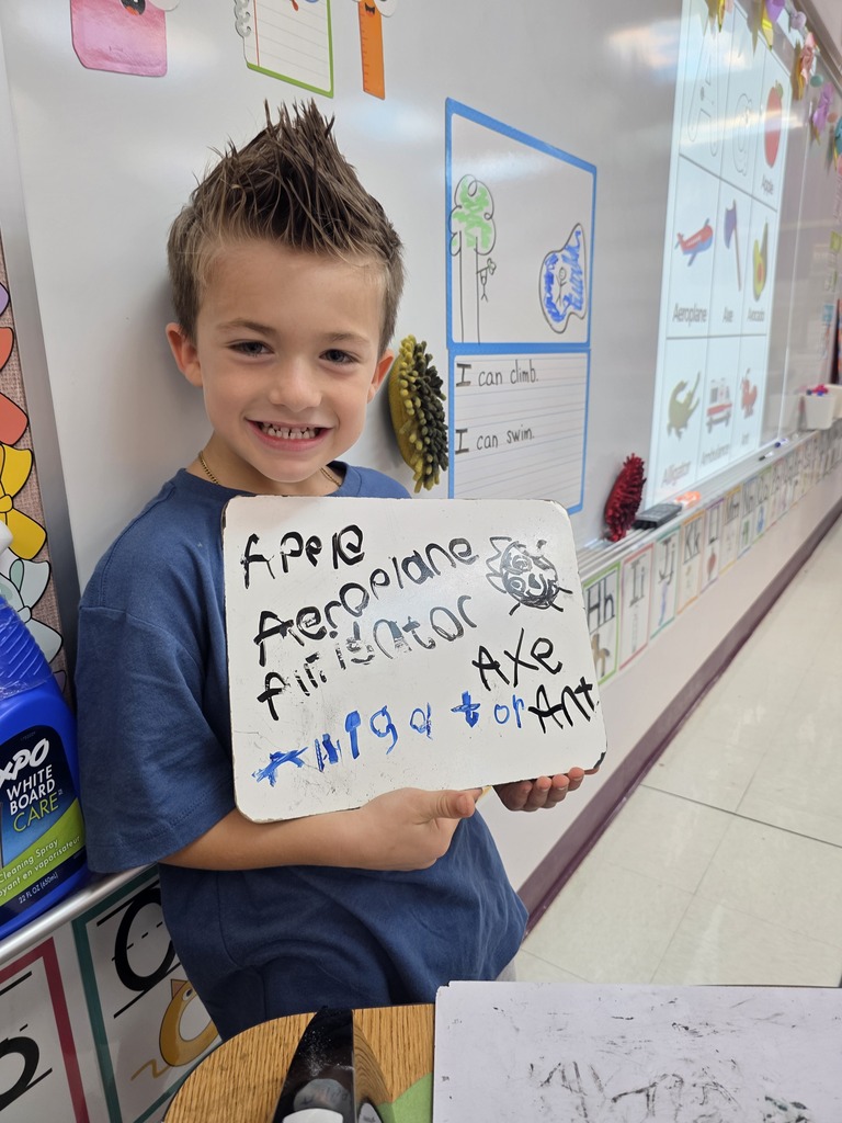 Boy holding sign with drawings and text. He smiles. 