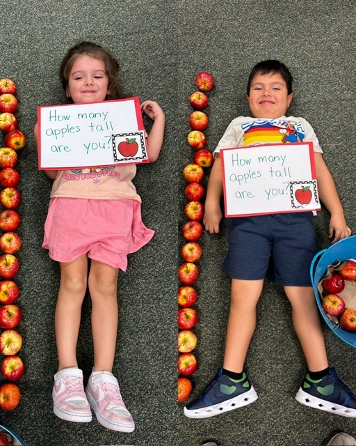 Two children lying on the floor with a row of apples, each holding a sign asking "How many apples tall are you?"