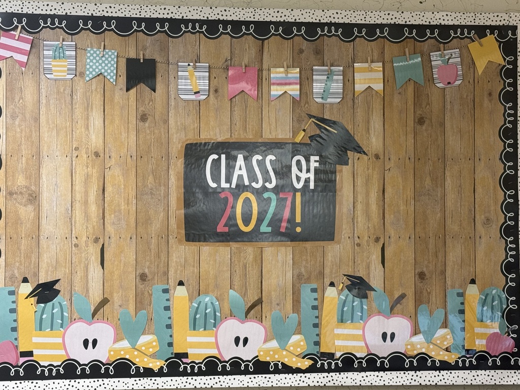 A bulletin board with a wooden background, a chalkboard saying "Class of 2021," and decorative elements like graduation hats, pencils, and apples.