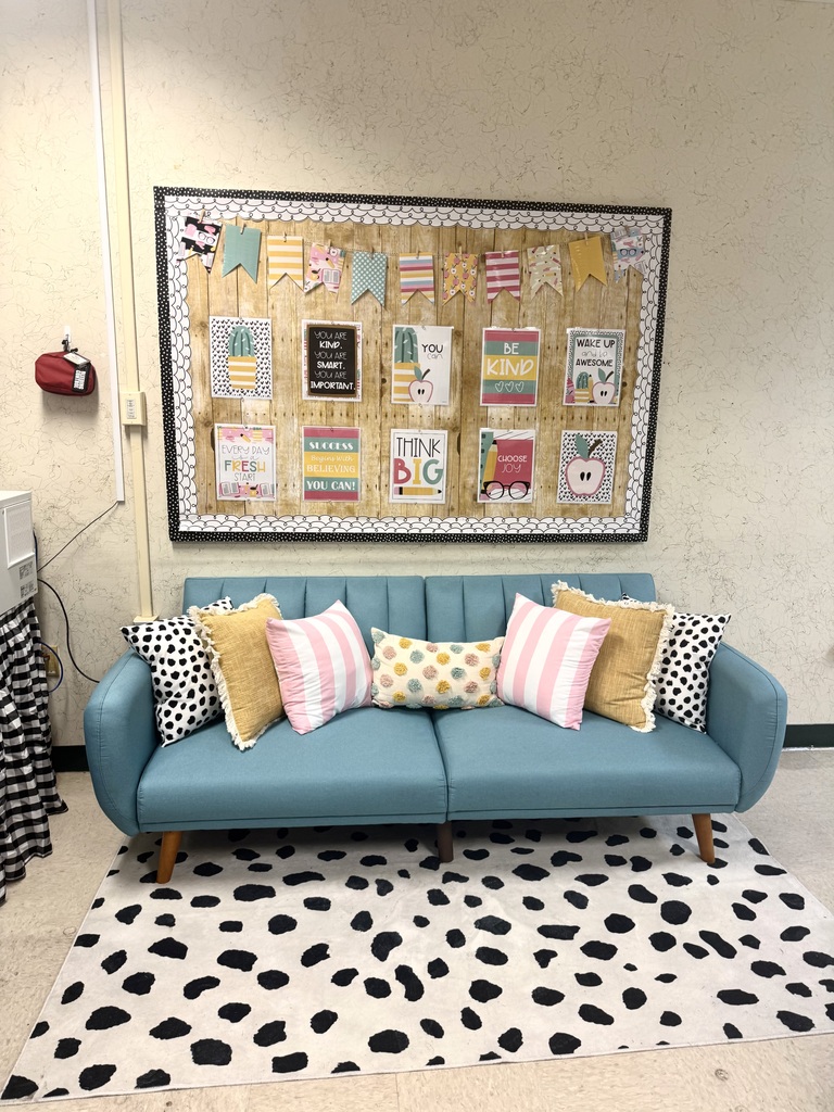 A room with a couch, colorful pillows, and a bulletin board. The rug has black and white spots.