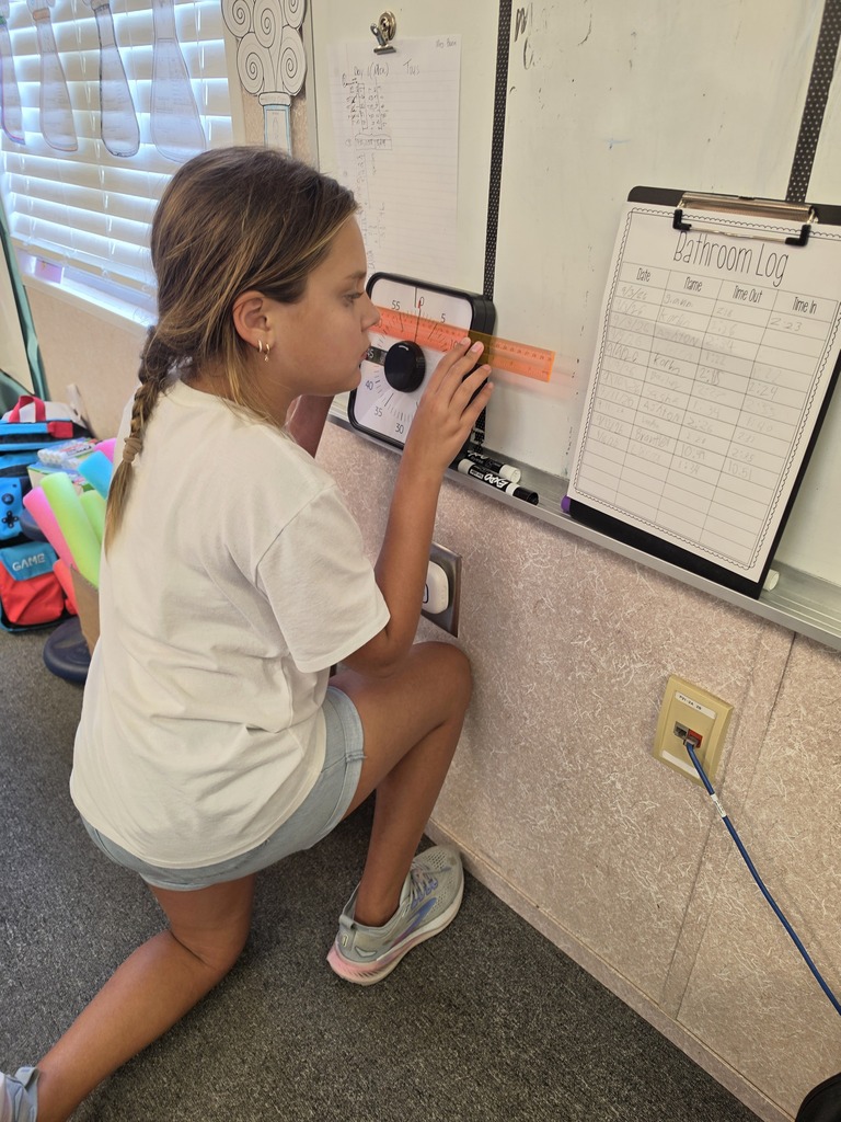A young girl sits on the floor using a classroom whiteboard. She wears a white shirt and shorts.