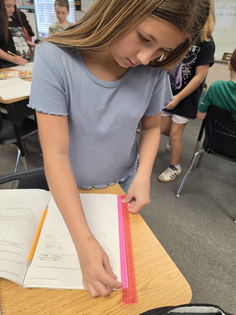 A girl in a blue shirt uses a red ruler to measure on a piece of paper.