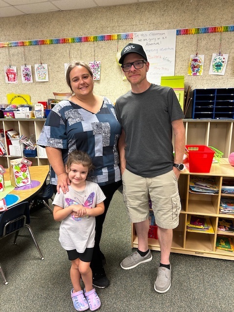 Three people in a classroom with a woman, a man, and a child. The child wears a butterfly shirt.