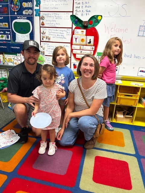 A group of five people, including two adults, smiles and poses for a photo in a classroom.