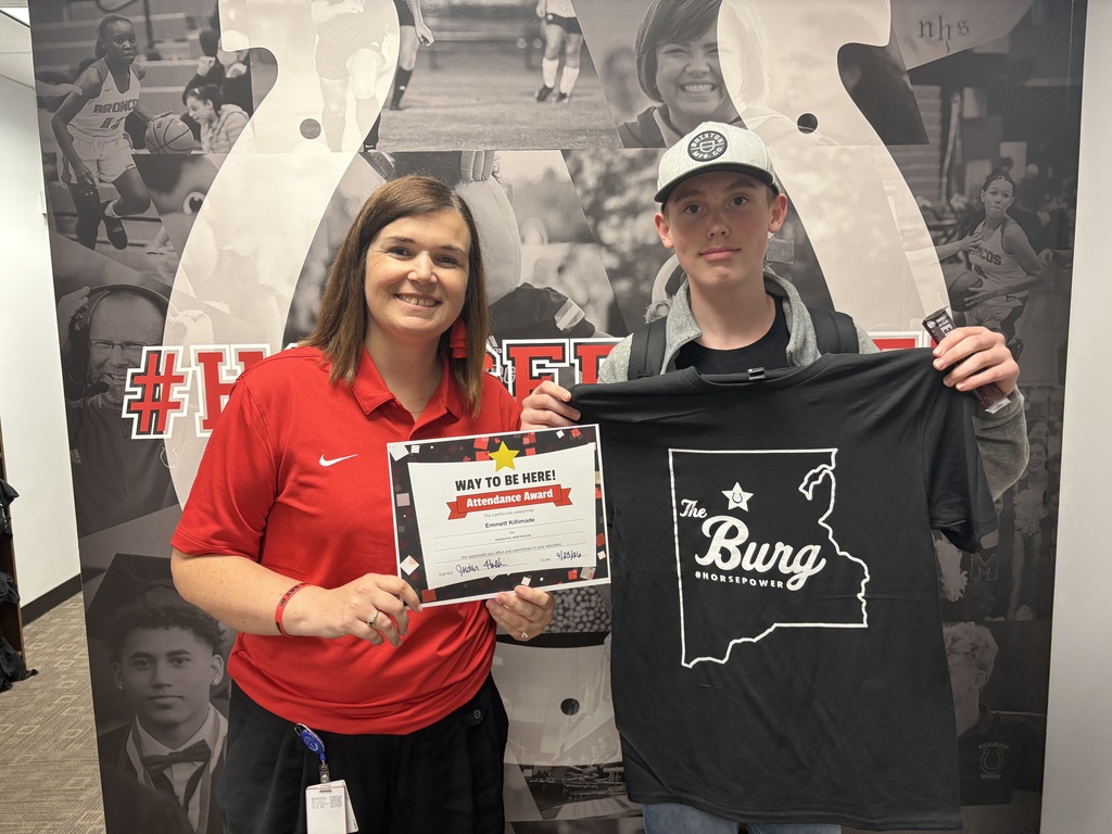 A woman and a boy stand in front of a wall, holding a certificate and a black T-shirt.