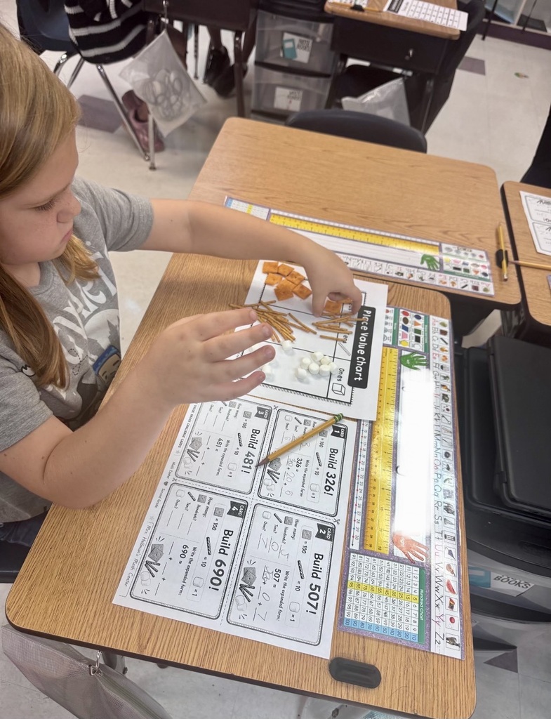 Child at a desk counting objects and writing numbers on a paper with a pencil.