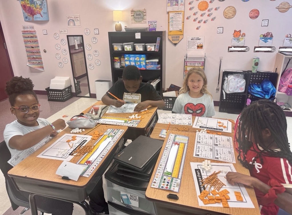Four students, two girls and two boys, sit at desks in a classroom, working on an activity.