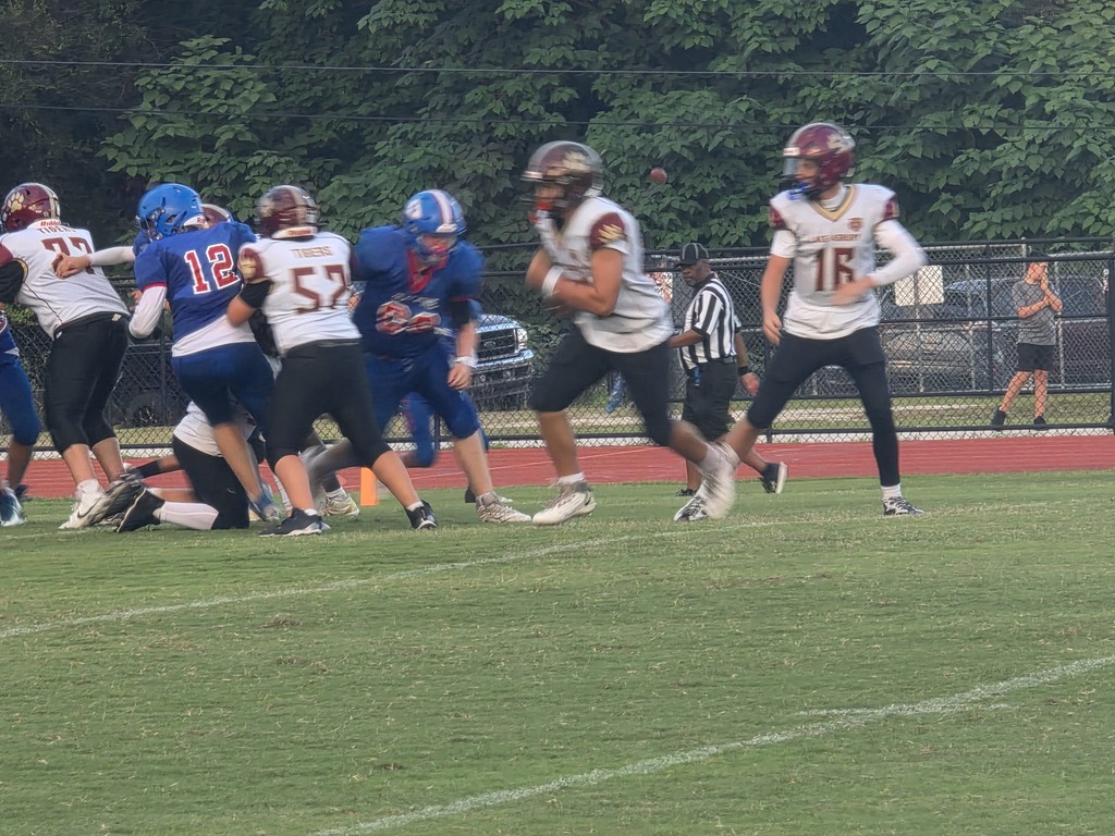 Players in numbered jerseys, helmets, and sneakers on a field. One player runs with the ball.