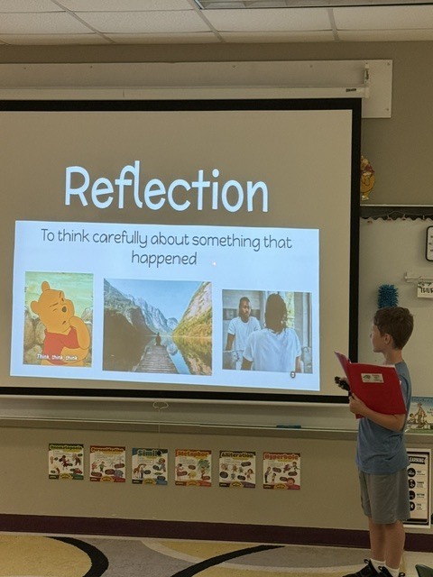 A young person stands in front of a classroom projector screen. The screen shows a slide titled "Reflection".