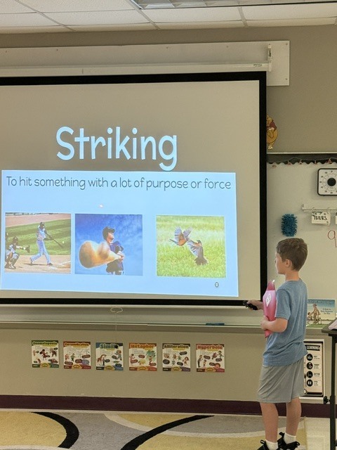 A boy stands in front of a projector screen in a classroom, presenting a slide titled "Striking".