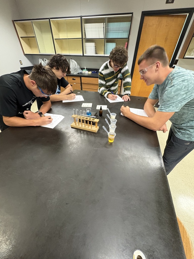 Four people in lab coats work at a lab table, with beakers, test tubes, and a beaker rack.