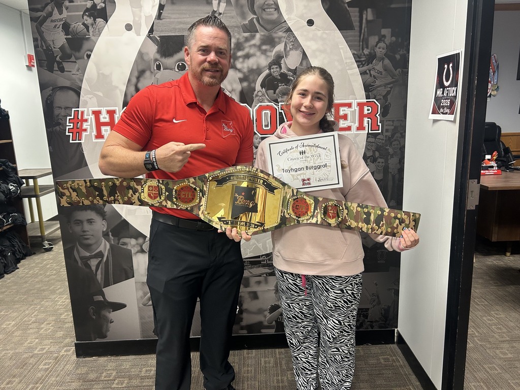 A man and a girl holding a belt, with the girl also holding a certificate. They stand before a large photo.