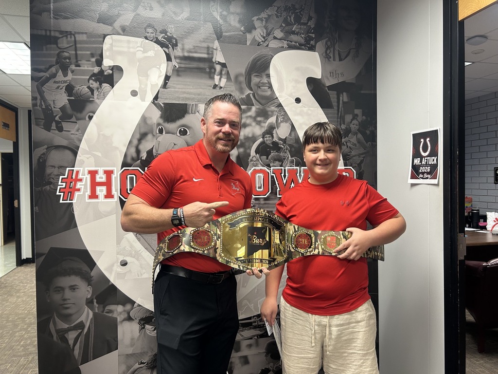Two individuals in red shirts and belts standing next to each other, in front of a sports-themed wall.