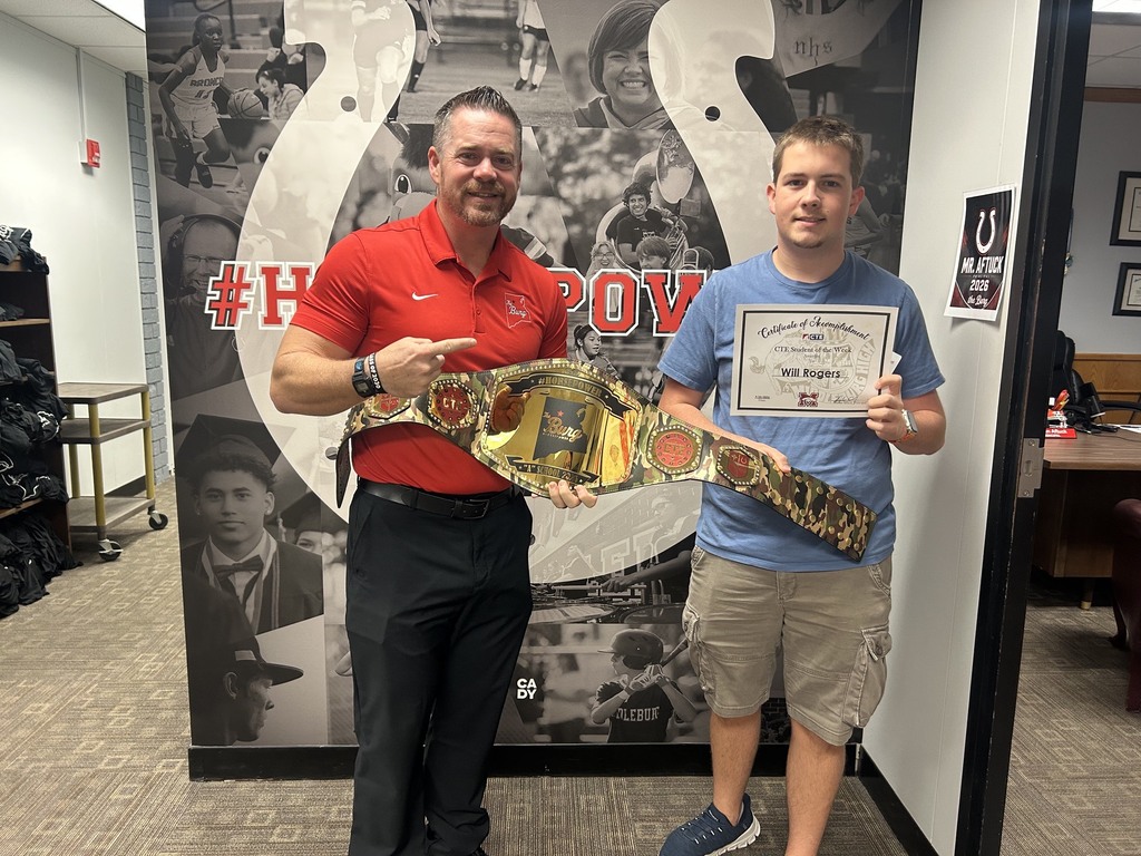 Two men pose in an office. One holds a belt, the other a certificate. Behind them, a mural depicts a collage of images.