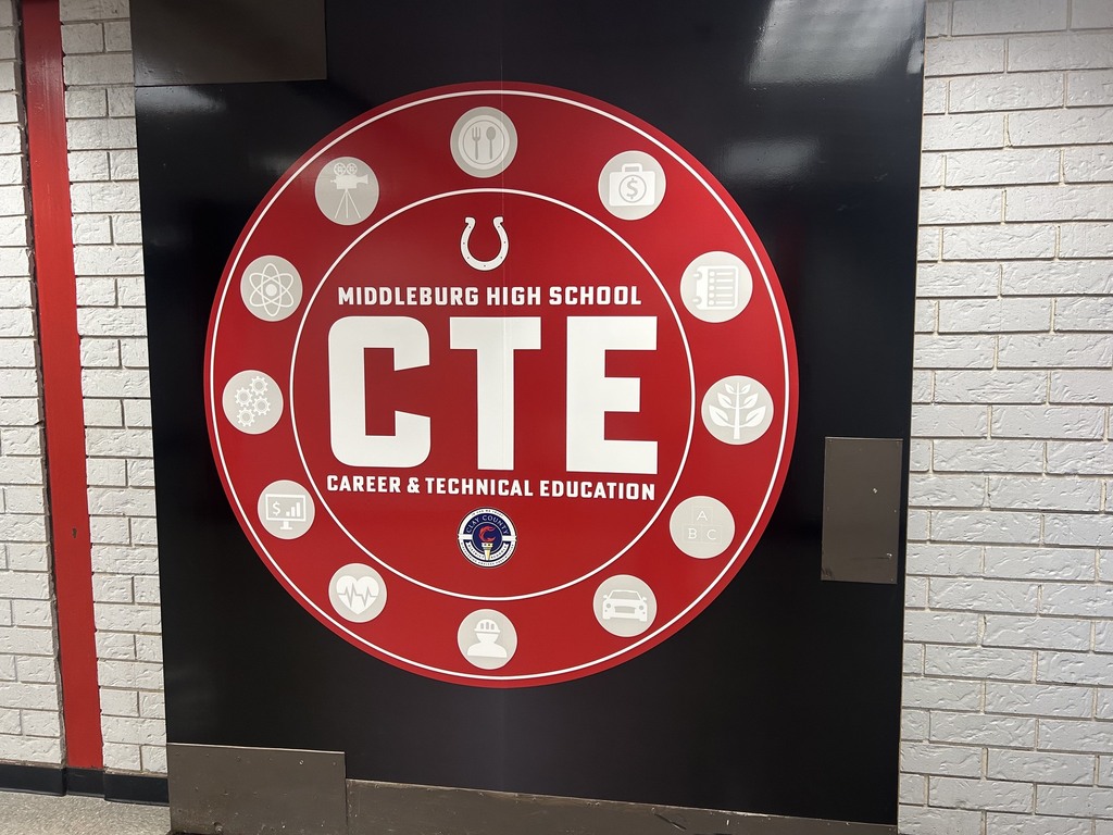 A red circular sign with white dots and "CTE" text against a white brick wall with red trim.