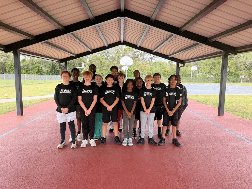 Group of young individuals in matching black shirts and shorts standing together on a red track.