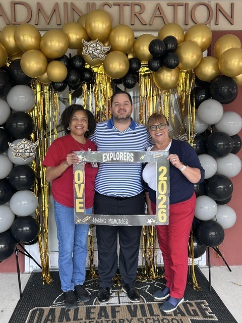Three people pose with a frame reading "Ove 2020" in front of a balloon backdrop.