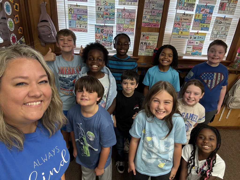 A woman and children pose together in a classroom, with various posters in the background.