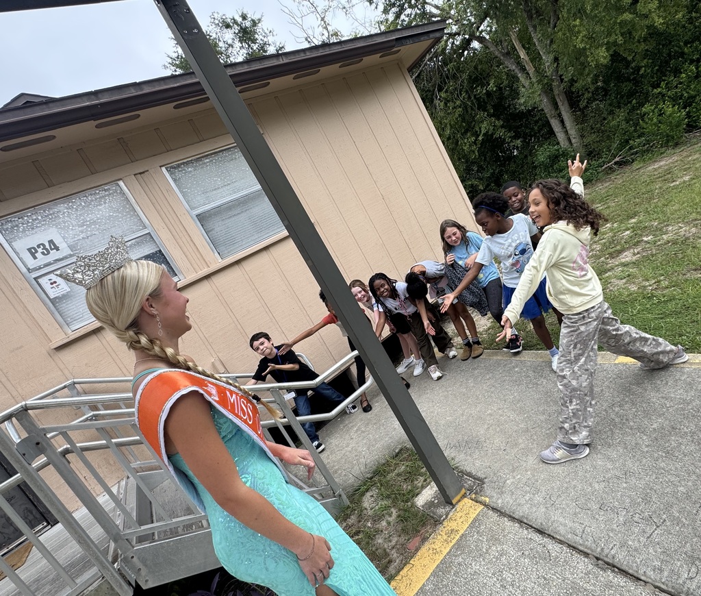 A group of individuals stand outside a house; a girl with a crown faces another person.