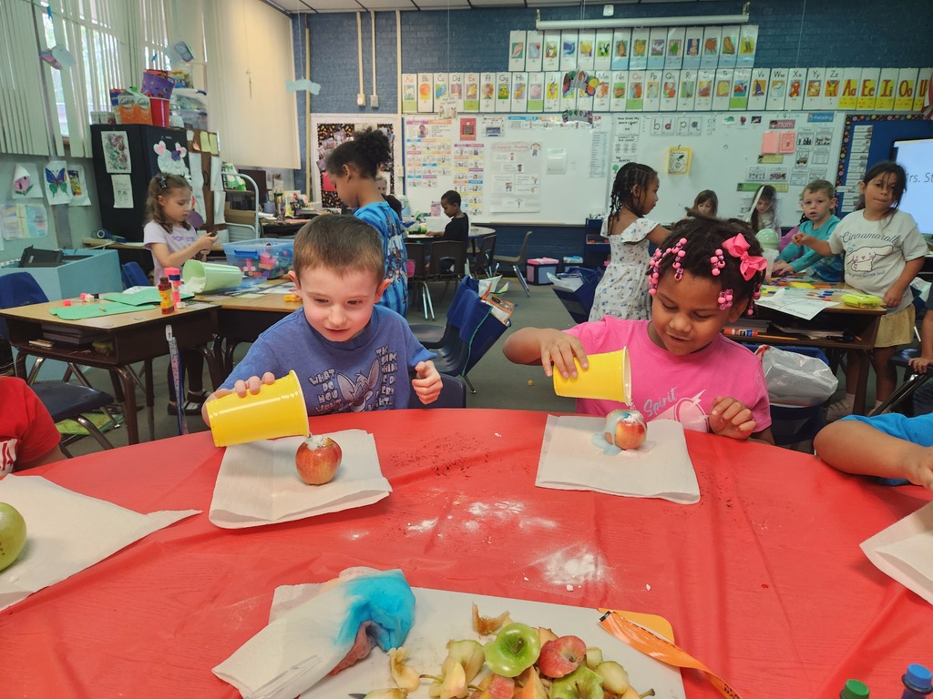 Children seated at a table in a classroom with apples and yellow bowls on the table.