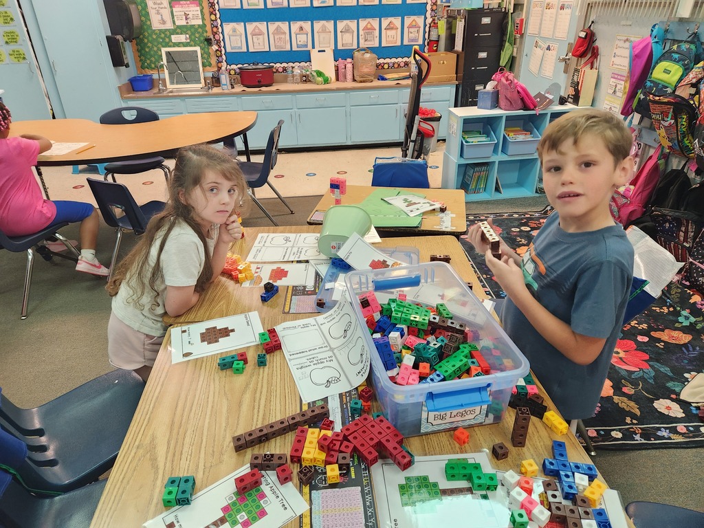 Two children focus on building with colorful blocks at a desk, surrounded by chairs and tables.