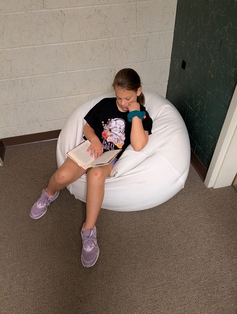Girl in black shirt and purple sneakers reading a book while sitting in a white bean bag.