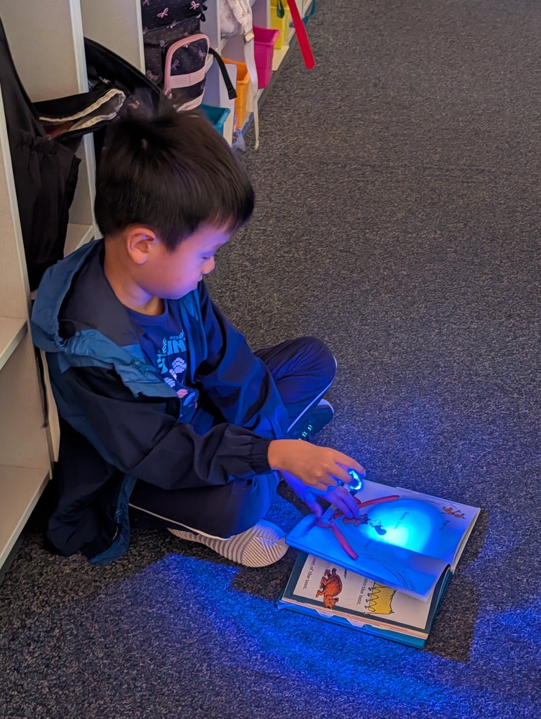 A boy sits on the floor reading a book, with a blue light illuminating the pages.