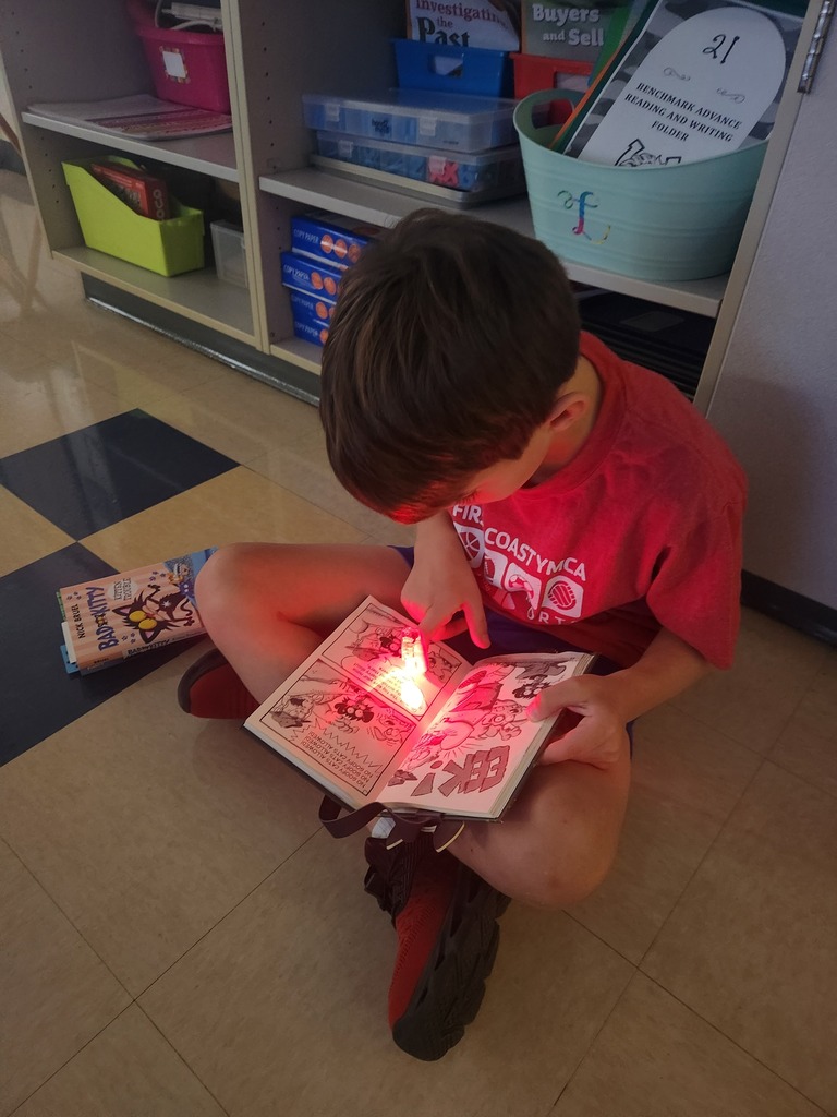 A child wearing a red t-shirt is sitting on the floor and focusing on a book.