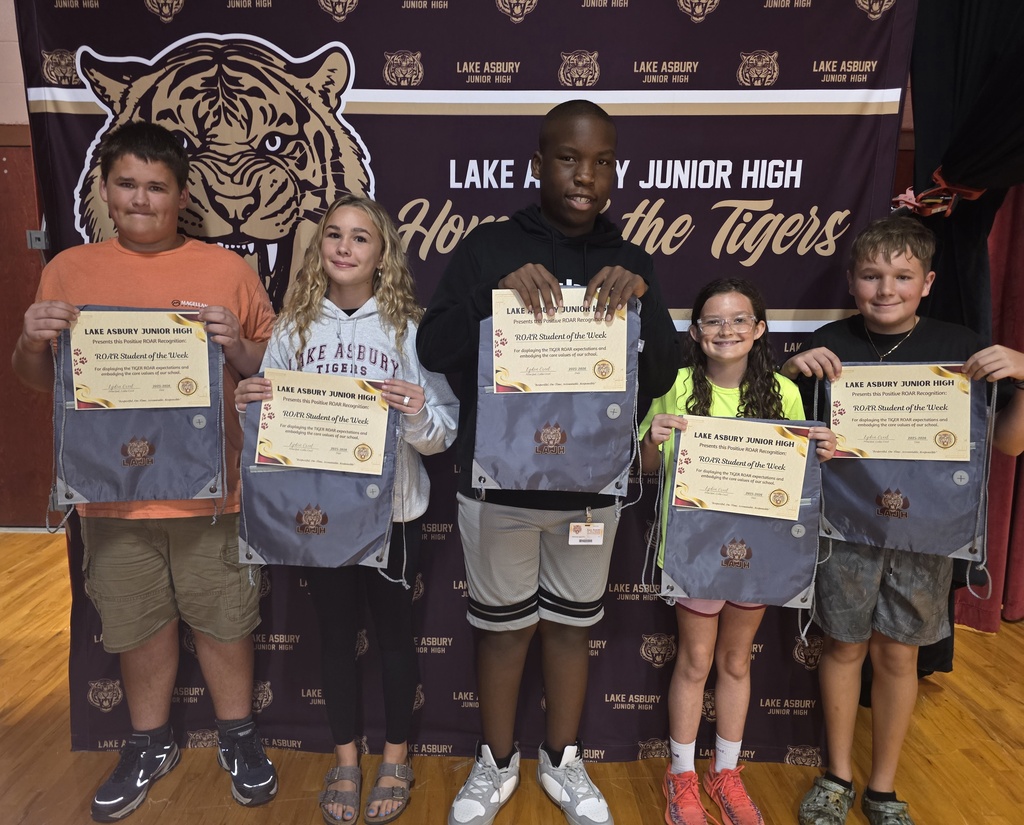 Six children in sports attire pose in front of a banner with a tiger mascot, holding certificates.