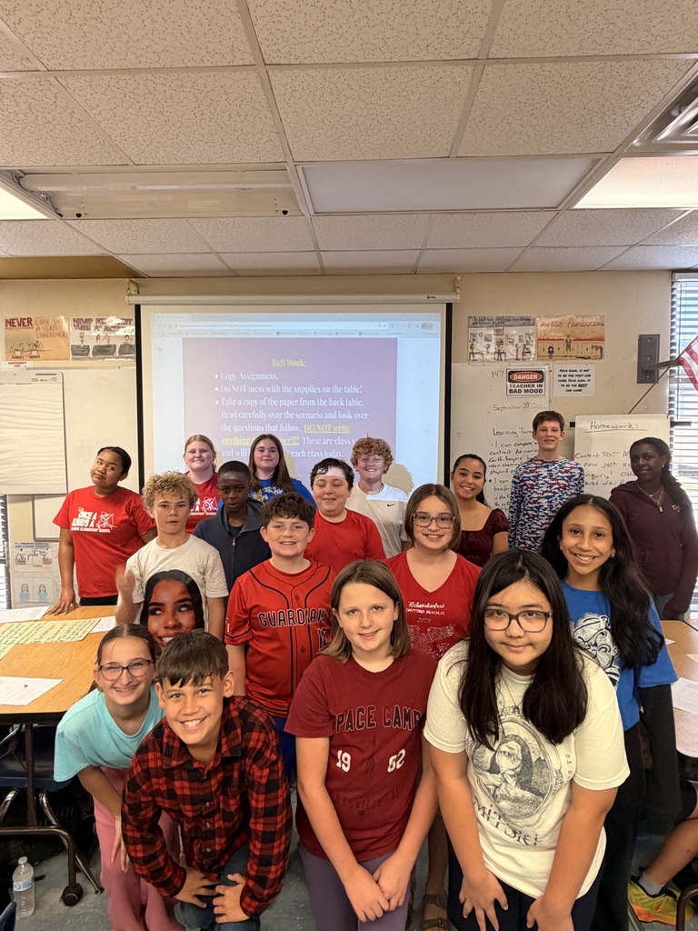 A classroom with students in red, blue, and white shirts posing for a group photo.