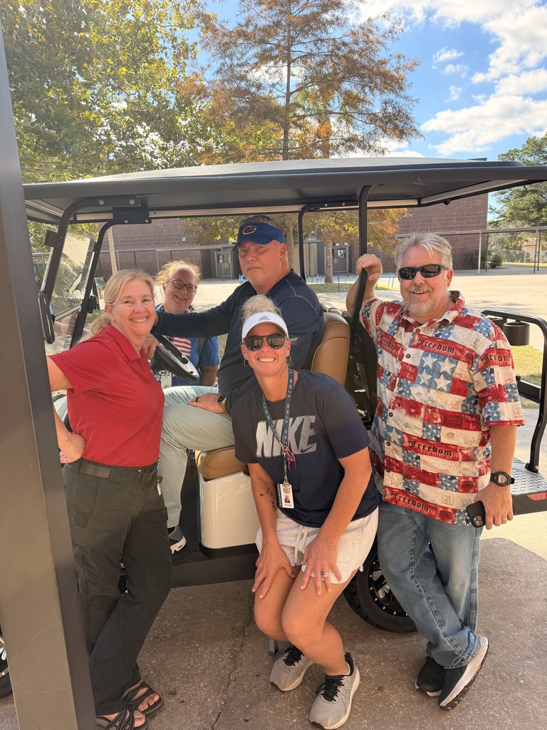 A group of five people in casual clothing, smiling and standing beside a golf cart in a parking lot.