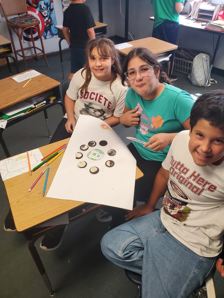 Three children with smiles on their faces. One holds a paper with buttons on it.