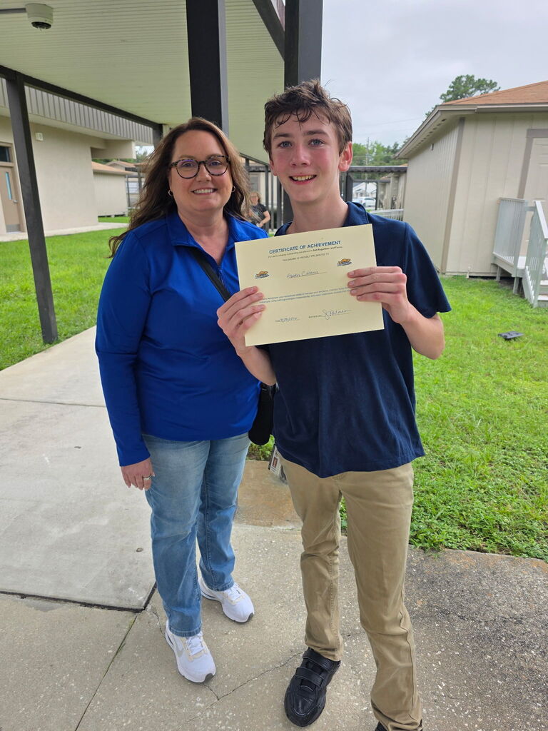 Photograph of Mrs. Palmer in jeans and a blue shirt and a male student holding an award
