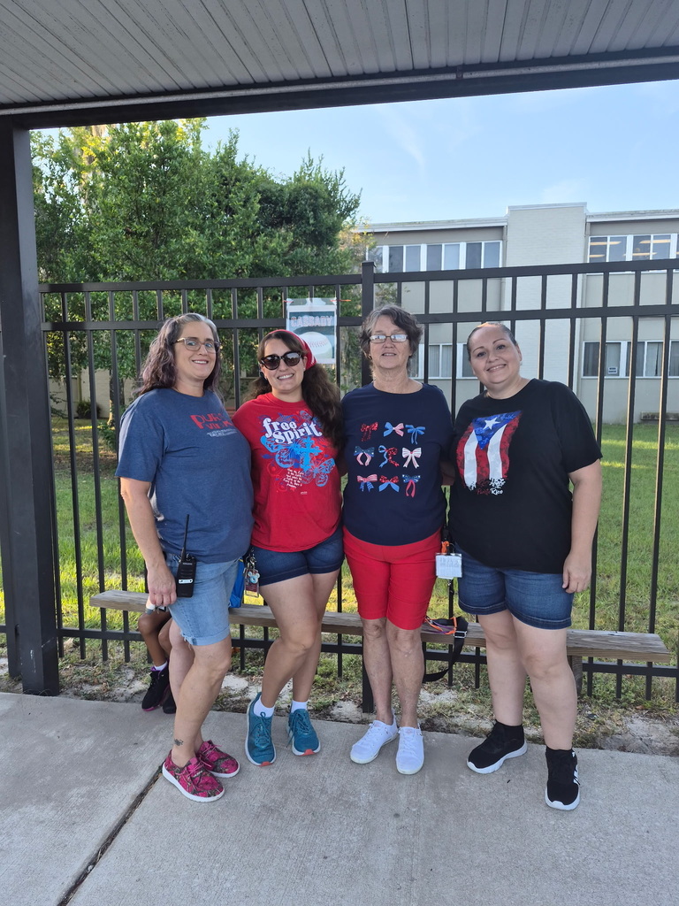 Four adult women, two wearing sunglasses, pose for a photo in front of a black fence.